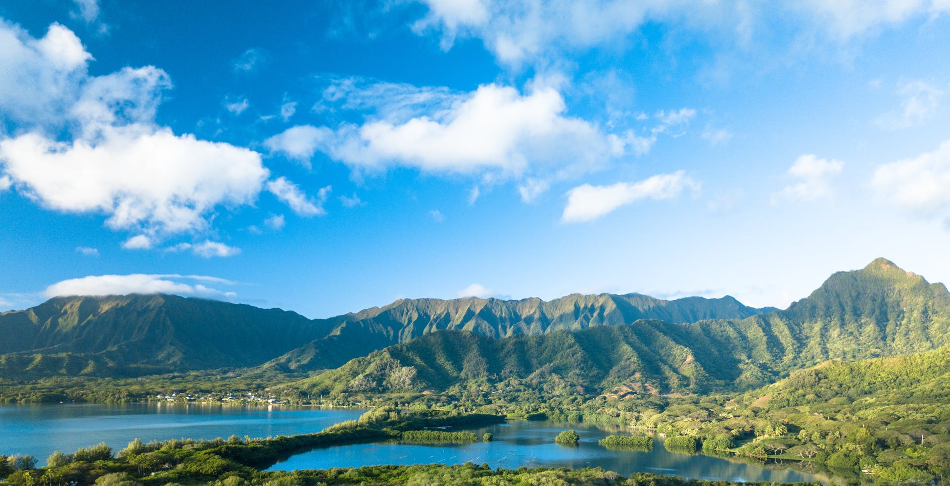 green forested mountain range under blue sky with clouds