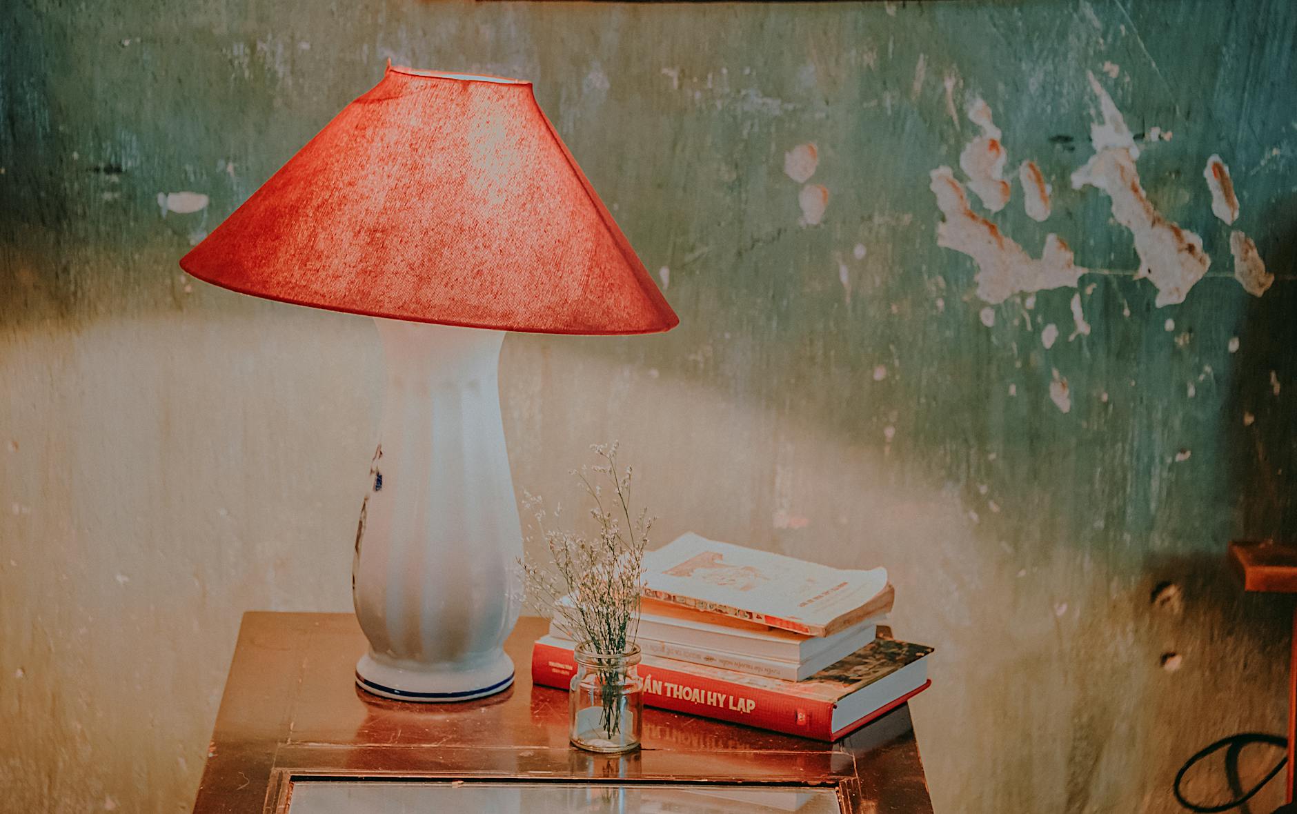 white and red table lamp assorted color books and white petaled flower in clear glass vase on brown wooden end table