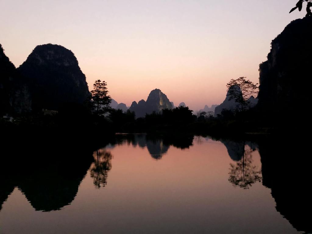 silhouette of trees and rock mountains near lake during sunset