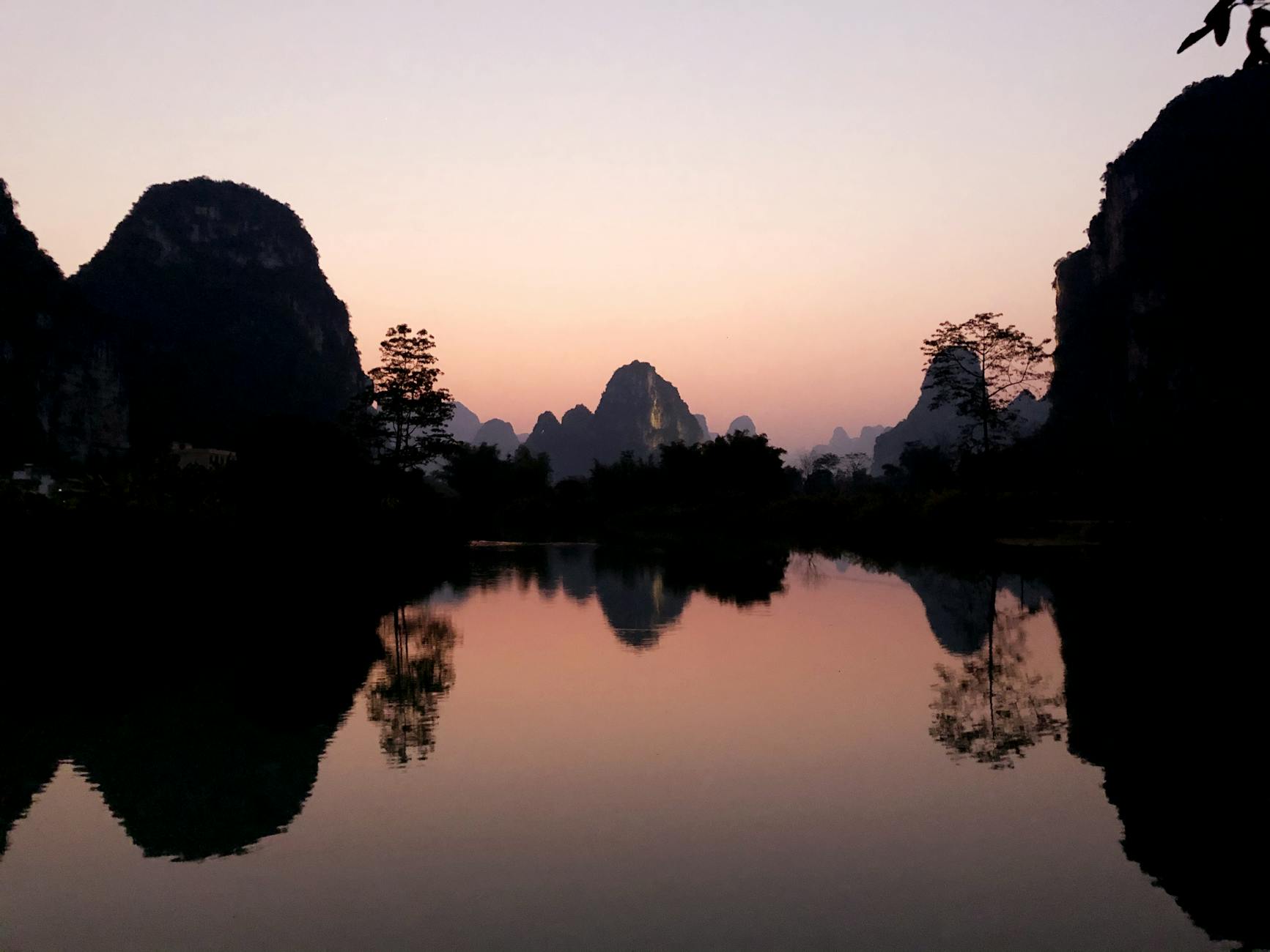 silhouette of trees and rock mountains near lake during sunset